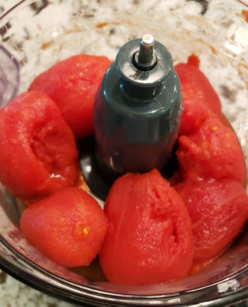 Photo of whole peeled tomatoes in the work bowl of the food processor